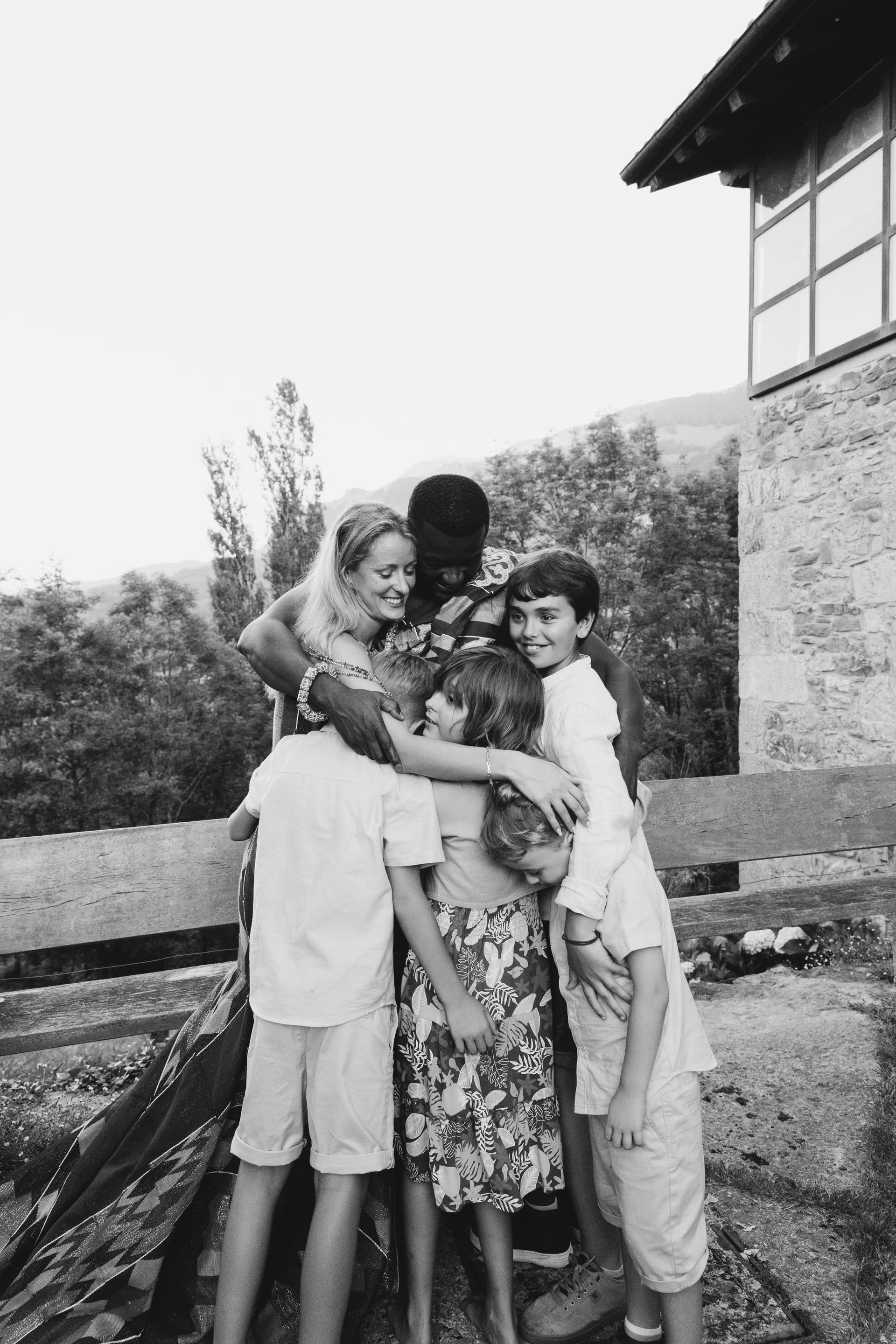 Un grupo de invitados jóvenes abrazándose delante de una casa, en blanco y negro