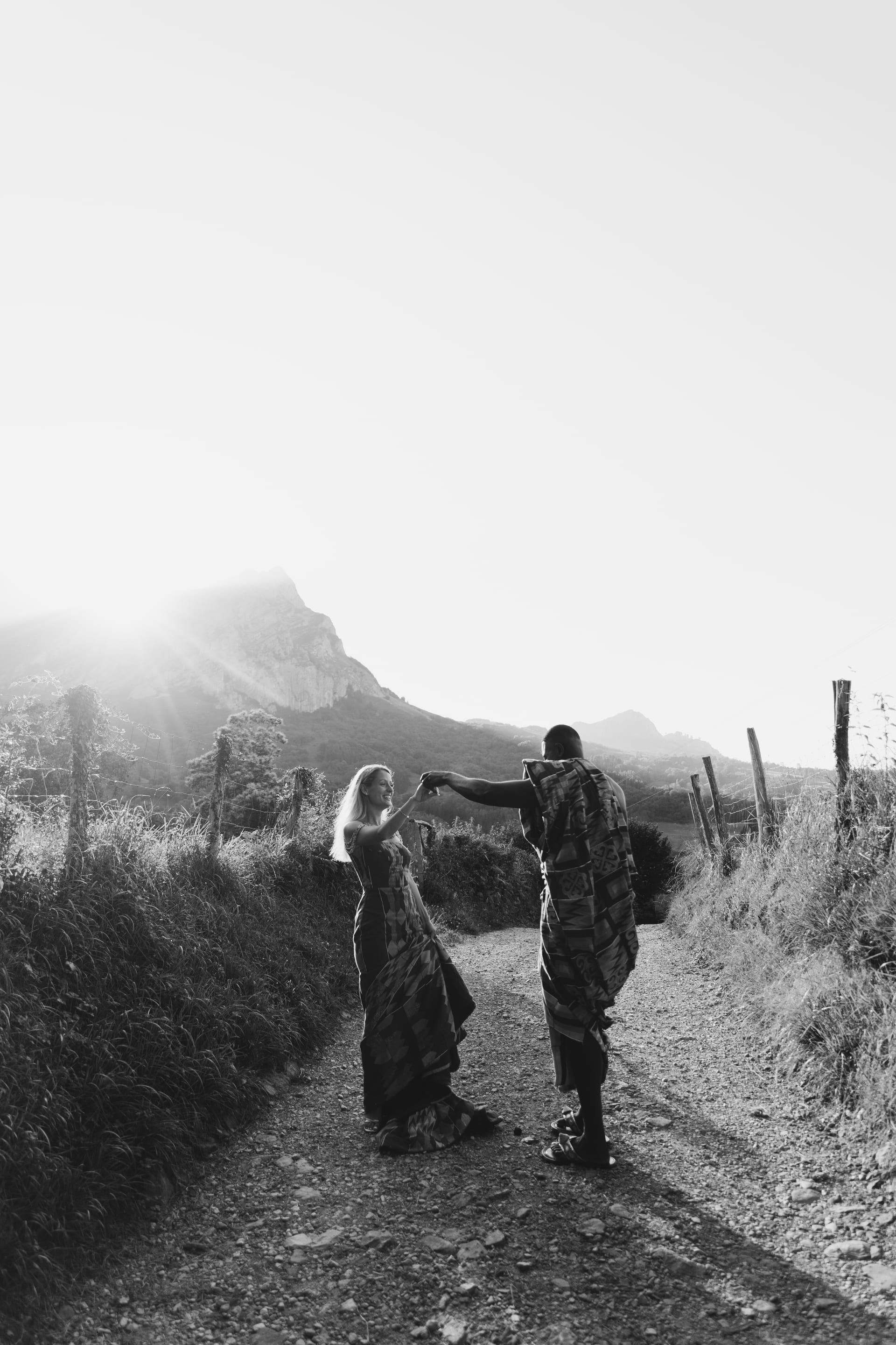 Dos figuras caminando por un camino de tierra hacia las montañas con niebla, en blanco y negro