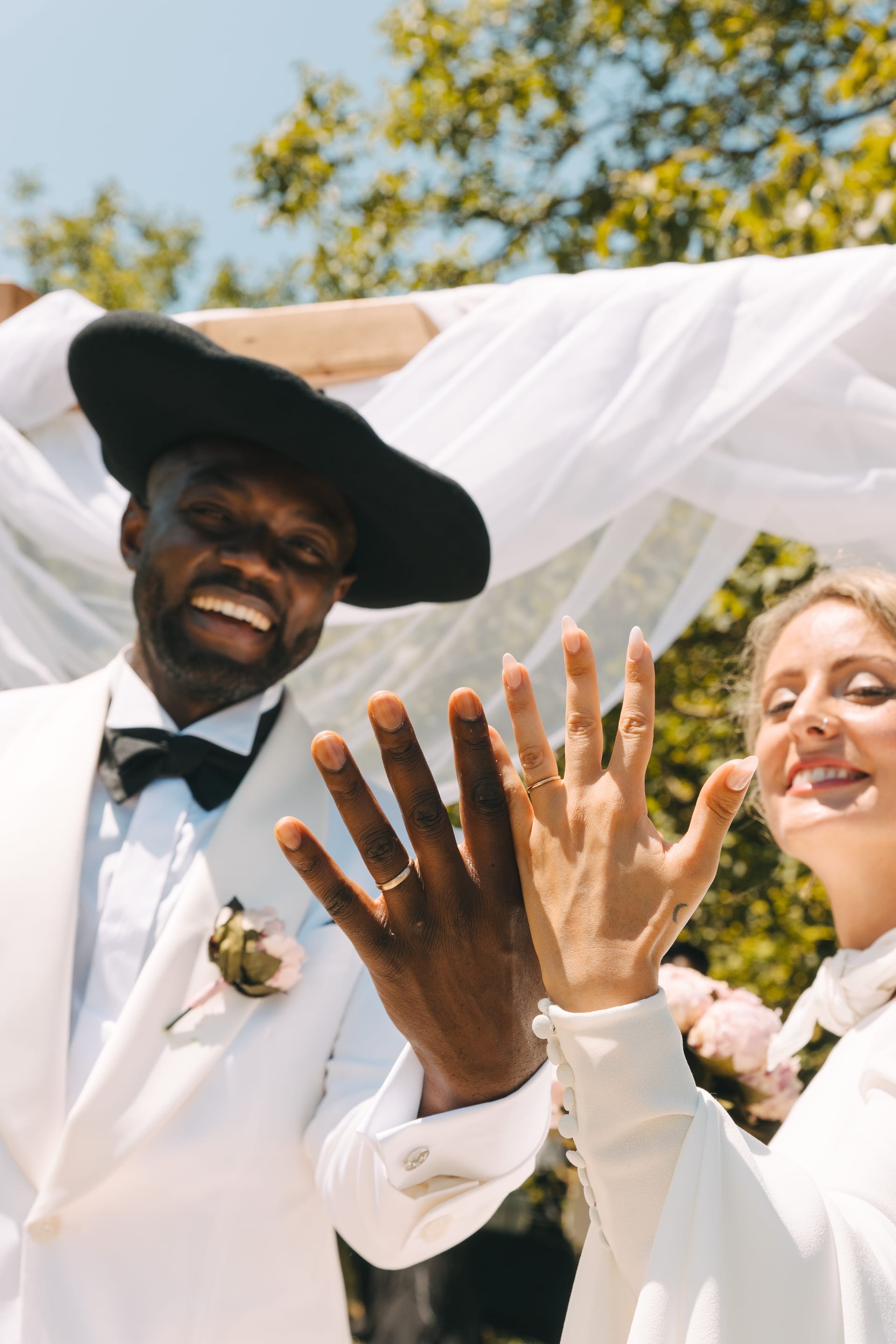 El novio con sombrero negro enseñando el anillo riendo, con la novia al lado