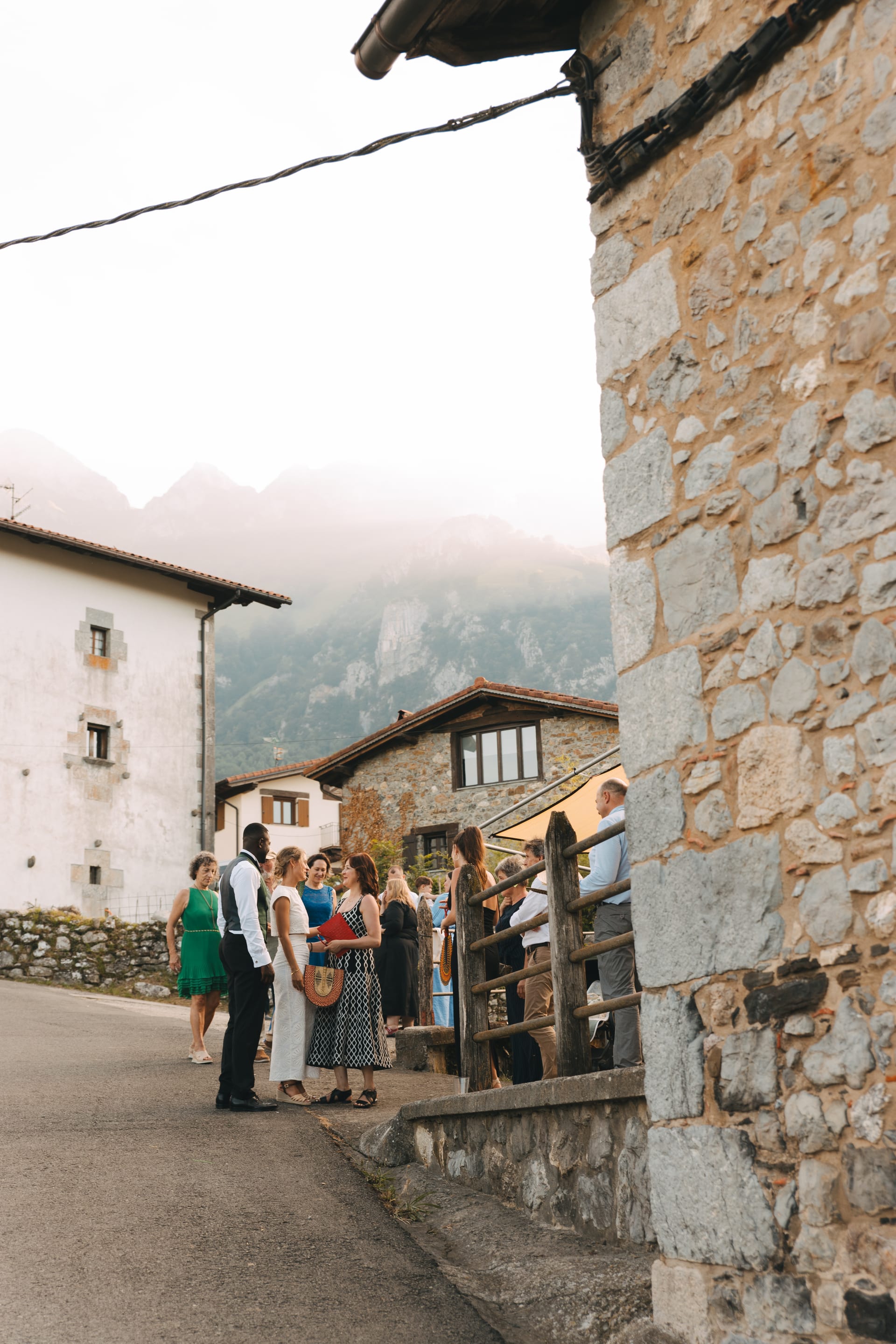 Invitados en la calle del pueblo entre casas de piedra, con la montaña con niebla al fondo