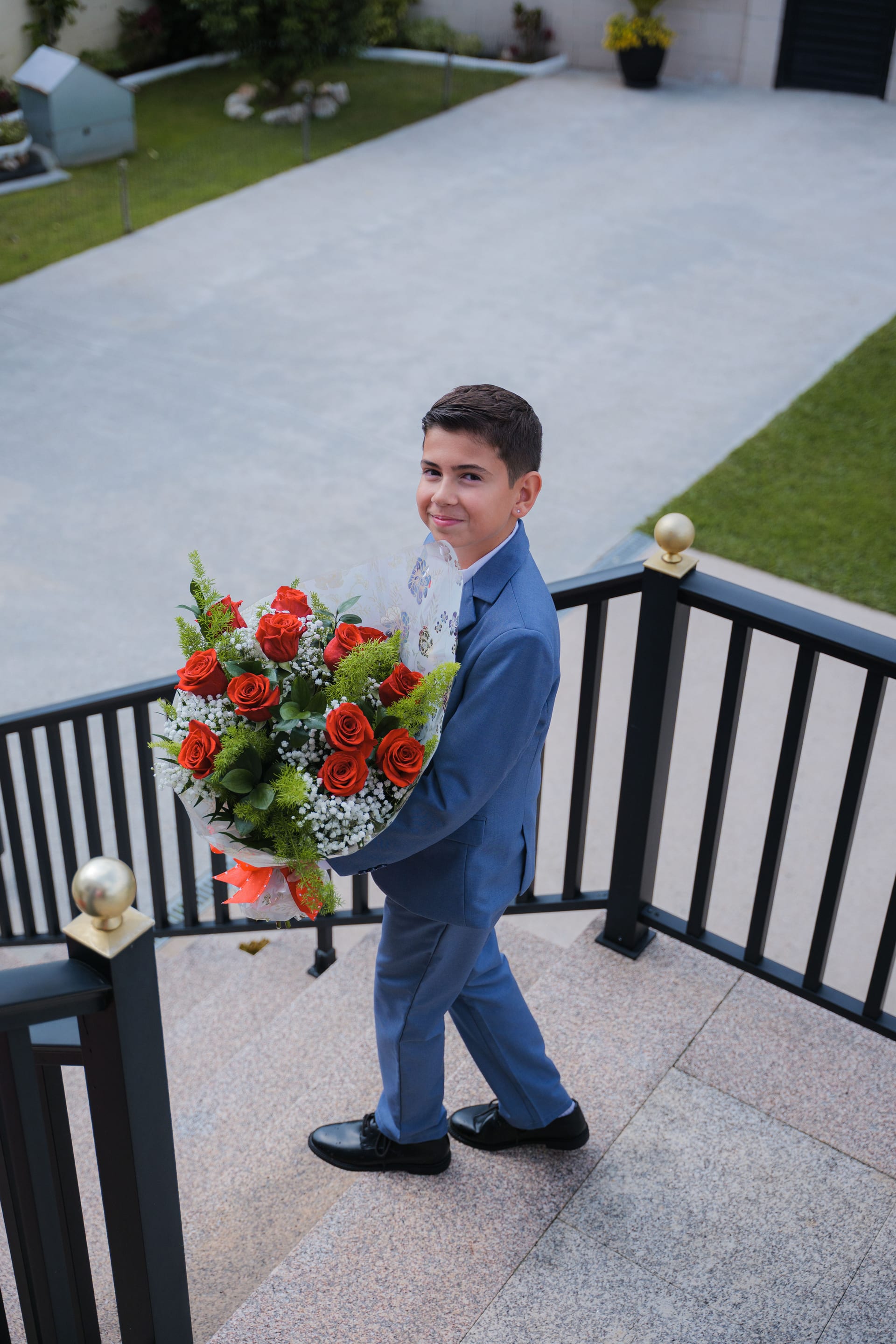 Un niño con traje azul con el ramo de rosas rojas