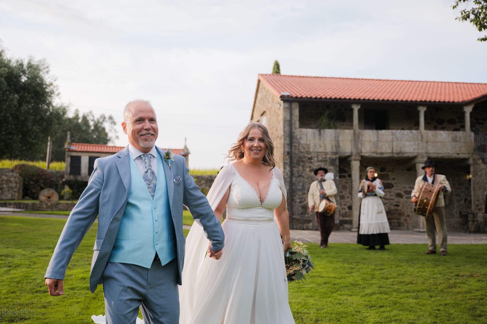 Los novios caminando por los jardines con los gaiteros detrás